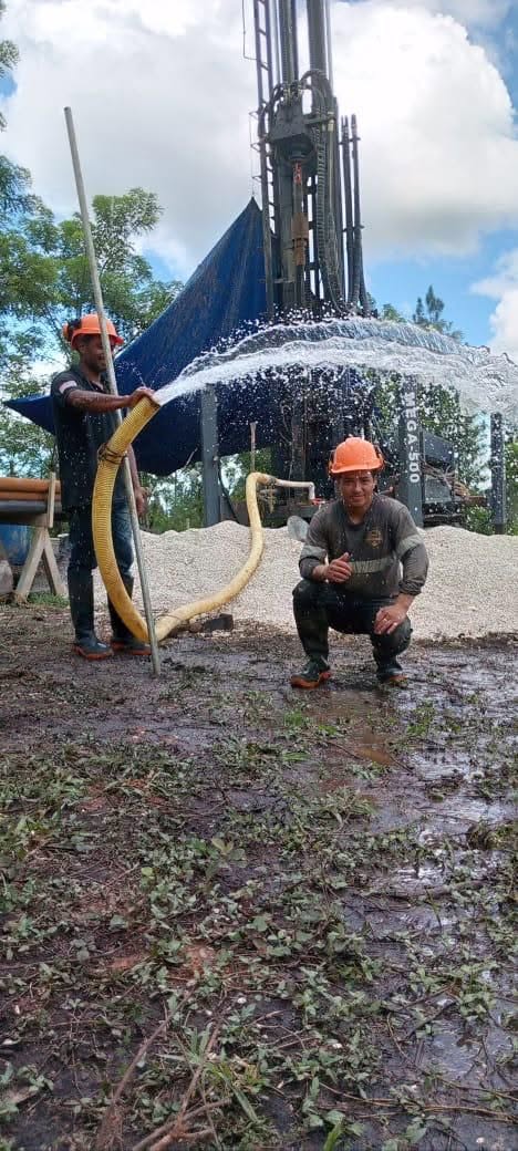 Personal de campo de Megapozos junto a la perforadora y una manguera con salida de agua